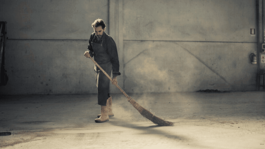 Worker sweeping a dusty warehouse with a broom