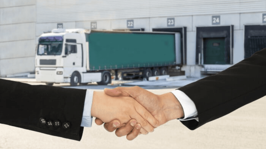 An image of two business people shaking hands in front of a warehouse