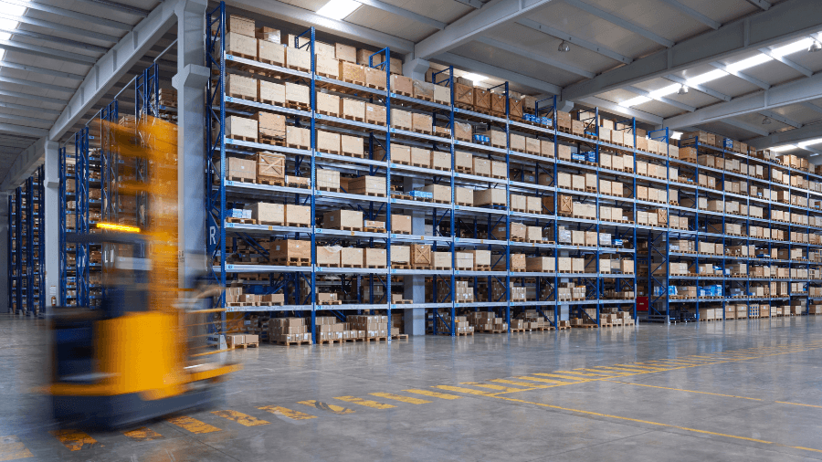 Photo of a forklift moving inside a warehouse, stacked with inventory