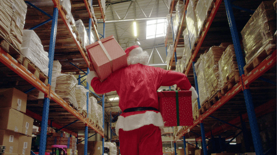 Santa carrying presents down a warehouse aisle