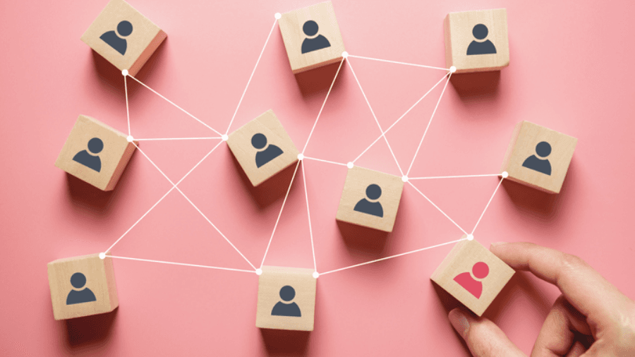 Block with people icons printed on them, sitting on a pink table top. The blocks are joined by lines to demonstrate the linking of people in an organisation.