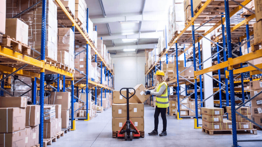 Worker in warehouse loading cartons onto a pallet on a manual fork.