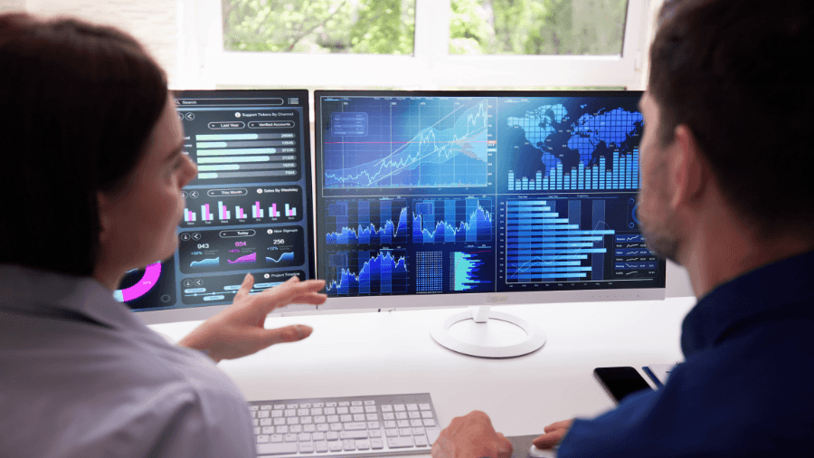 Two people looking at and discussing computer screens with data, charts and graphs.