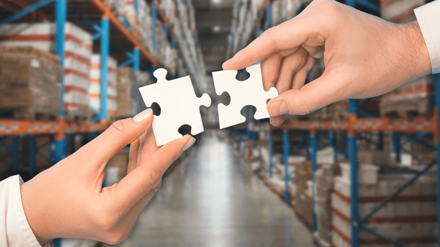 Puzzle pieces being held and placed together in the air. In the background is an image of the inside of a warehouse.