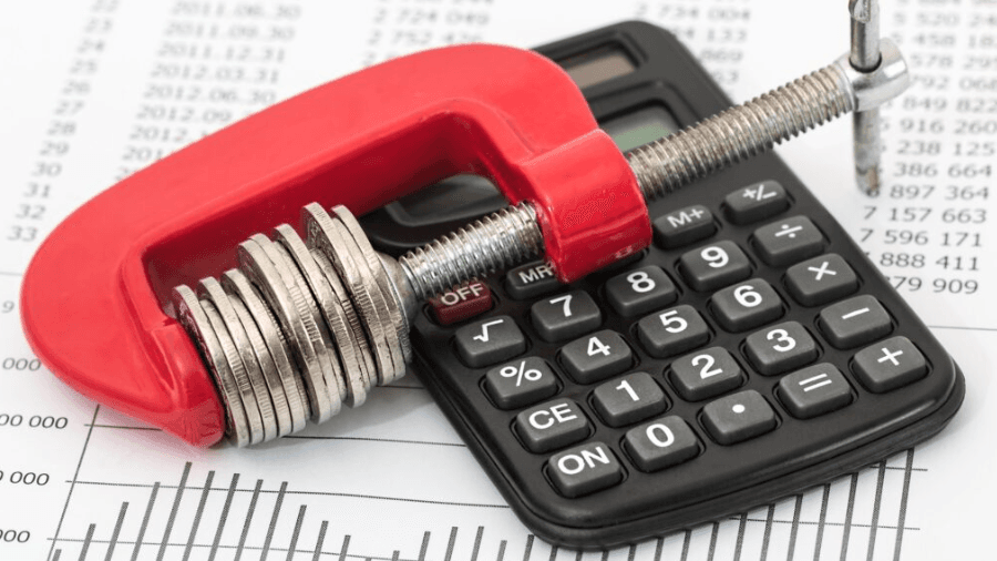 Calculator and vice with coins clamped in it to illustrate saving money.
