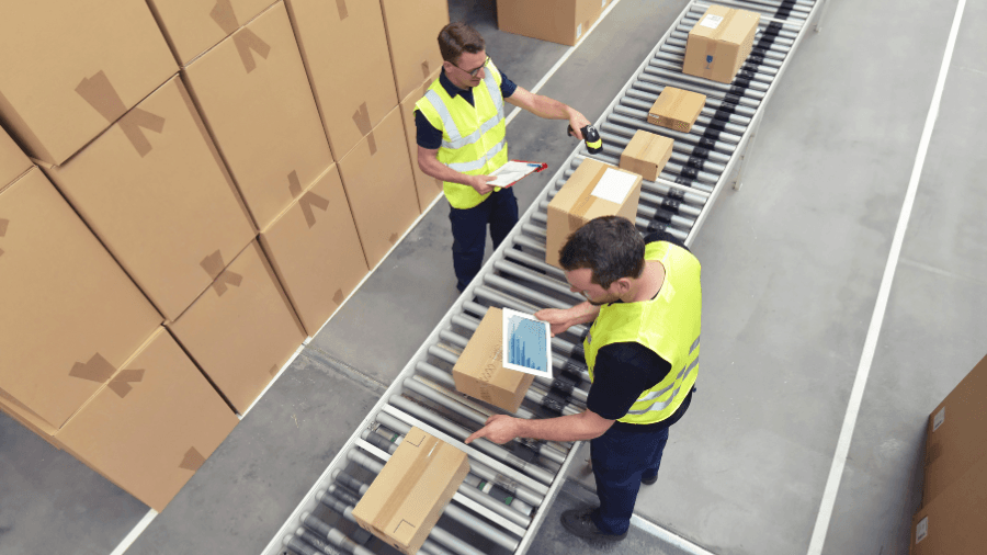 Two warehouse workers at a conveyor belt system, checking orders