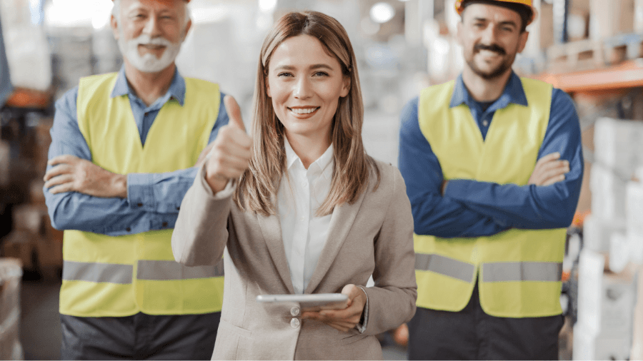 Women in foreground with a thumbs up gesture, with two men in the background in safety vests.