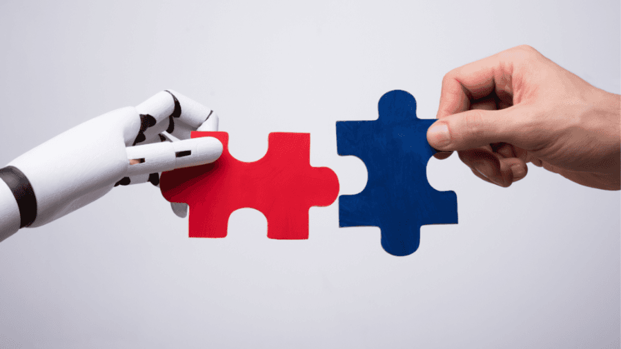 Robot arm holding puzzle piece and human hand holding another puzzle piece, bringing them together in the centre to join them.