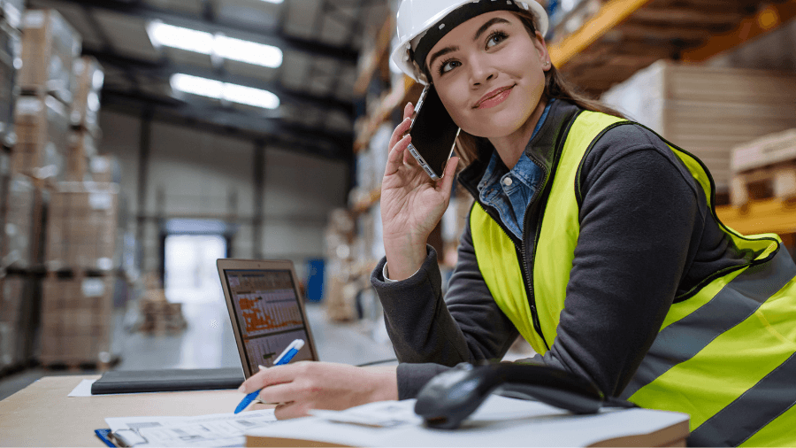 Woman on phone in a warehouse setting with laptop and paperwork in front of her, reviewing rate card and other data.