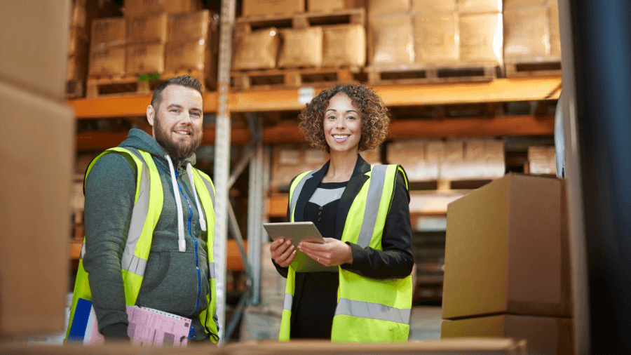 Two workers in warehouse, smiling at the camera.